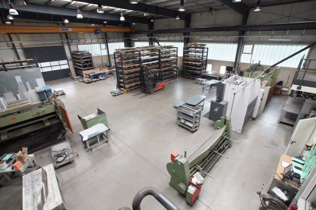 Große, moderne Produktionshalle mit Maschinen, Werkbänken, Lagerregalen und Gabelstapler – Blick von oben auf den Fertigungsbereich.