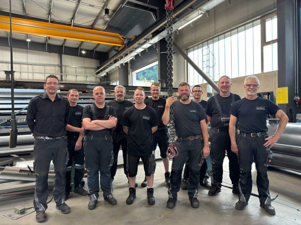 Das Werkstatt-Team von Goldsaat Agrartechnik steht in der Produktionshalle und blickt lächelnd in die Kamera.
